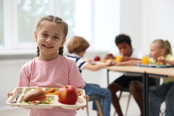 Fototapeta na wymiar Little girl with tray of tasty food in school canteen