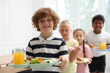 Little kids with trays of tasty food in school canteen, selective focus