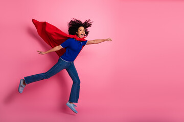 Energetic young woman in superhero pose with flowing red cape against pink background, celebrating empowerment and fun. © deagreez