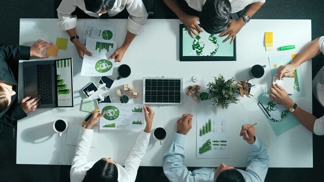 Top down view of business team discussing about using clean energy and sustainable investment at meeting table with wind mill, document with environmental graph and wooden house model. Alimentation. - Powered by Adobe