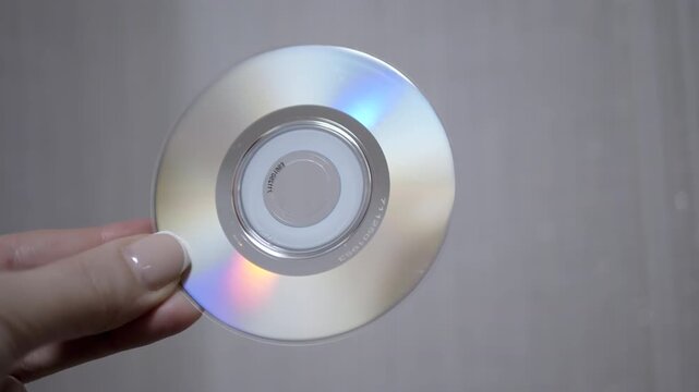 A hand holds a CD, showcasing its iridescent surface and reflecting light. Great for technology, music, or data-related projects.