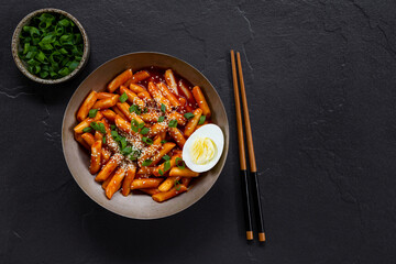 Korean street food, tteokbokki with egg and sesame in a bowl on dark background top view copy space for text