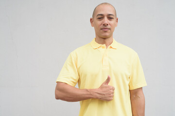 Portrait of bald Hispanic man with thumb up gesture against plain white background wall