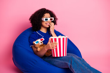 Young woman enjoying leisure, wearing stylish sunglasses, holding popcorn bucket, seated on bright...