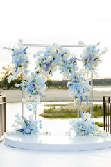 The wedding arch for the wedding ceremony, decorated with white and blue flowers, stands on the water background