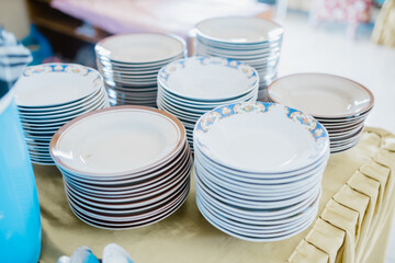 Stacks of ceramic plates arranged neatly on a table. Piles of white and patterned dishware used for...