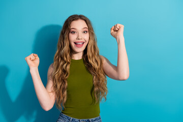 Happy cheerful young woman in green top celebrates success on blue background
