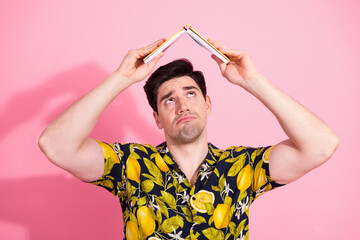 Man holding a book as a hat on a pink background wearing a tropical print shirt in a humorous pose