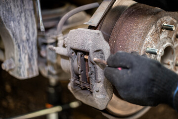 A mechanic removes the retaining elements of a brake caliper while replacing brake pads on a car