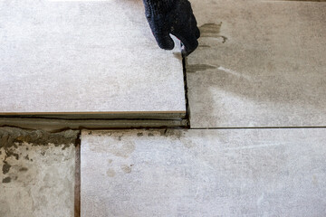 A worker lays gray ceramic tiles during a floor renovation, ensuring precise alignment with plastic...