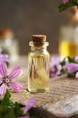 A bottle of common mallow essential oil with blooming mallow plant