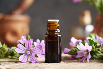 A bottle of common mallow essential oil with blooming plant