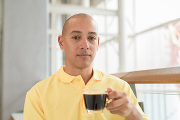 Mature Hispanic bald man sitting at a cafe holding coffee cup