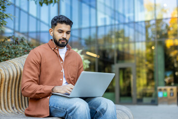 Man working outdoors with laptop in urban environment wearing earphones