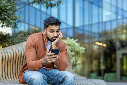 Man sitting outdoors using a smartphone with a thoughtful expression - Powered by Adobe