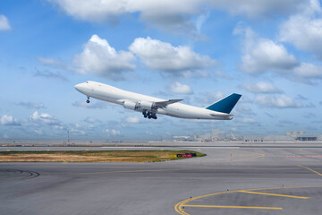Four engine, cargo airplane is shown taking off from an airport runway. The sky is blue with...