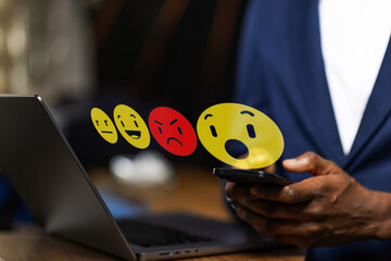 African businessman holding smartphone with floating emojis, manage online reviews, customer...