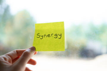 Hand holding sticky note with synergy written on it