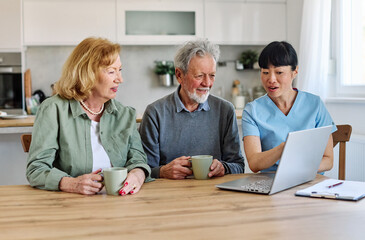 Female caregiver with senior woman and man using laptop at home