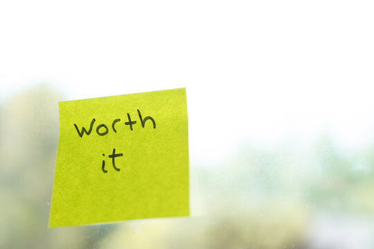 Yellow sticky note saying worth it on blurred background