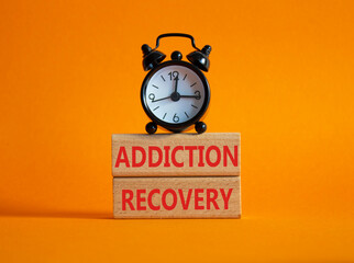 Addiction Recovery symbol. Concept words Addiction Recovery on wooden blocks. Beautiful orange background with alarm clock. Medicine and Addiction Recovery concept. Copy space.