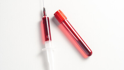 A syringe with a red liquid in it is next to a red tube. The syringe is full of blood and the tube...
