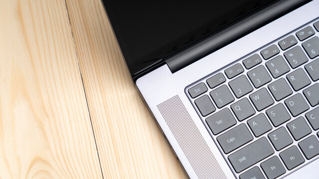 A laptop is open on a wooden table. The keyboard is grey and the laptop screen is black