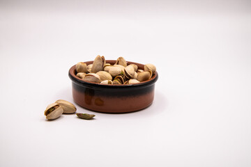 Small terracotta dish filled with pistachio nuts on a clean white background, perfect for illustrating healthy snacks, nutrition, and natural food concepts.
