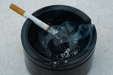 Burning cigarette in a black ashtray