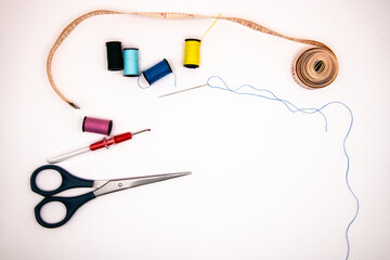 Sewing essentials on a white background: colourful cotton reels, scissors, threaded needle, tape measure, and stitch picker, perfect for crafts, tailoring, and DIY projects.