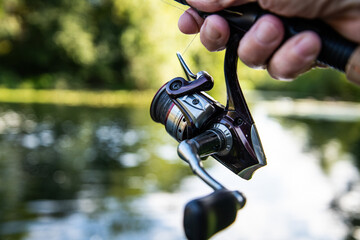 Fishing rod and reel held in hand, ready to cast over a calm river with water and nature in the...
