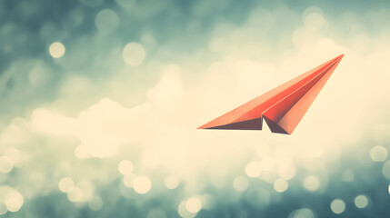 Red paper airplane soaring in a blurred sky with bokeh effects.