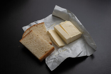 A piece of fresh butter wrapped in wrapping paper on a black background. Spreading butter on bread....