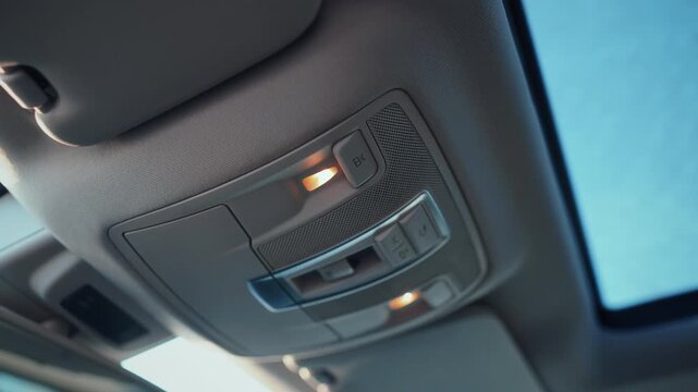 Close-up view of illuminated overhead console in modern car interior showing reading lights and control buttons under panoramic glass roof &ndash; premium automotive design detail emphasizing functionality 
