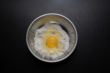 A pile of flour and a broken egg in a bowl. View from above. Making dough from delicious wheat...