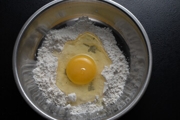 A pile of flour and a broken egg in a bowl. View from above. Making dough from delicious wheat...