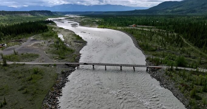 Approaching a bridge across the turbulent river crossed by the black car. Travel by the wild Alaska. Aerial view.