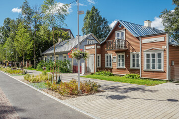 Traditional wooden houses on a quiet residential street with landscaped greenery, paved sidewalk, and clear blue sky in a peaceful suburban neighborhood in Parnu, Estonia, Europe
