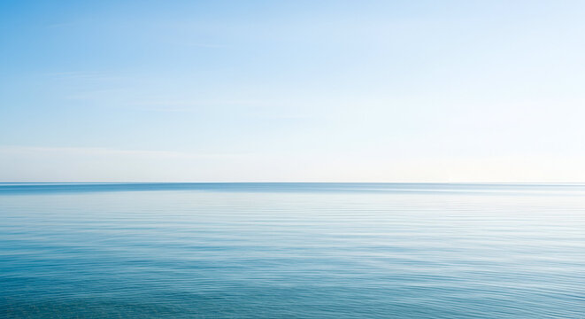 A wide-angle shot of calm blue ocean meeting a clear bright sky, minimalist composition, neat horizon line, clean natural background. - Powered by Adobe