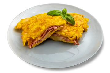 Omelette stuffed with ham and potatoes  with basil leaves in gray porcelain plate isolated