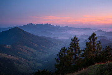 Obraz premium Majestic mountain range landscape with fog-filled valleys and a vibrant sky at dusk, creating a serene and atmospheric scene.