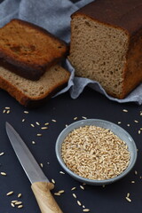 Rustic still life with dark bread slices wheat grains and kitchen knife on dark background