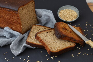 Rustic still life with dark bread slices wheat grains and kitchen knife on dark background