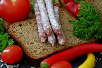 Rustic still life with bread salami vegetables and herbs on dark background