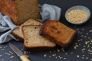 Rustic still life with dark bread slices wheat grains and kitchen knife on dark background