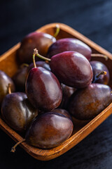 Ripe plums in bowl on black table.