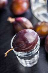 Plums and distilled alcohol on black table. Plum brandy shot.