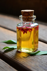 Glass bottle with yellow liquid and red flowers and cork stopper on a wooden surface with green leaves