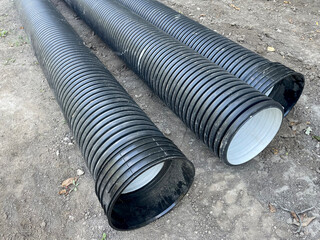 Large black corrugated plastic drainage pipes lying on the ground at a construction site, used for...