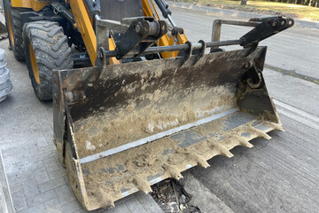 Close-up of a heavy construction loader bucket with teeth, dirty from recent work, attached to a...
